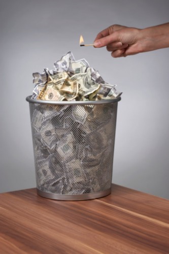 Person holding burning match over wastebasket full of dollar bills