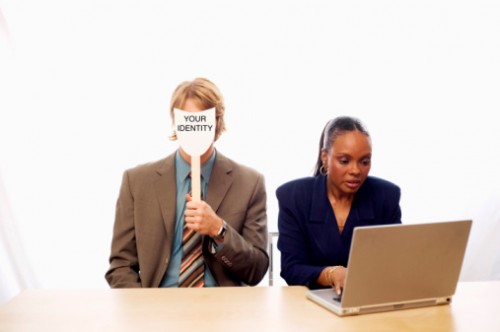 A women using a laptop next to man with mask symbolizing identity theft