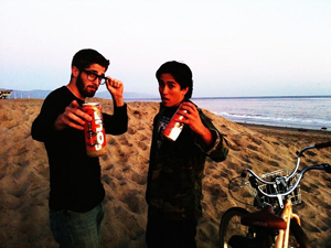 A couple of dudes on a beach flashing their Four Loko cans.