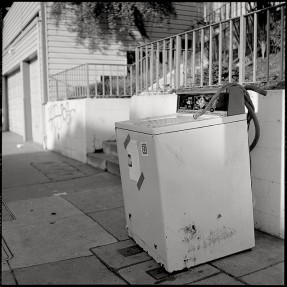 A broken down clothes washing machine on a city sidewalk.
