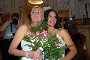 Two happily married women in wedding gowns with bouquets in hand.