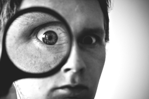 s&p_investigation Close-up of a man's eye peering through a magnifying glass. Veins are clearly visible in the magnified eyeball.