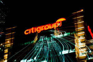 Nighttime photo of a Citigroup office building with lens flare that blurs the amber light of the corporate logo.