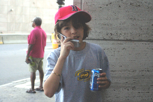 kids_cell_phones A nine-year-old boy talks on a cell phone. He's holding a Pepsi can in his other hand, and there's a red Boston Red Sox baseball cap on his head.