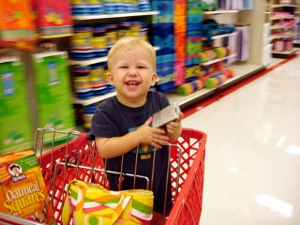 A young boy sits in a grocery store shopping cart. He's holding a cell phone.