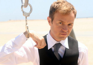A man in business attire is handcuffed to a pole in the middle of the desert.