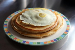 A colorful plate with pancakes and egg on top.