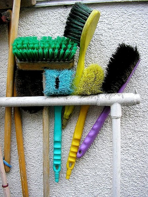 An assortment of cleaning brushes and brooms that are hung up and waiting for use.
