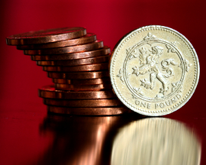 frivolous_spending Leaning stack of U.S. pennies beside a one pound English coin.