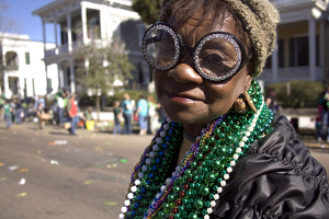 An elderly African-American woman at a St. Patrick's Day parade. She's clad in green beads and related holiday bling.