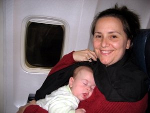 A woman seated on an airline, sleeping infant in her lap.