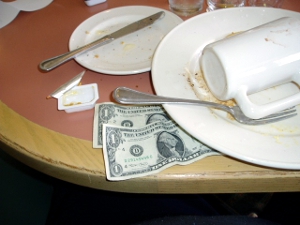 A couple of dollars gratuity left under a plate at a restaurant.