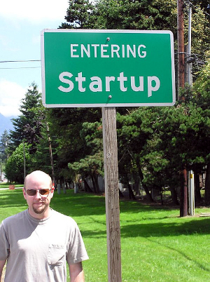 Man standing next to a street sign that reads, “Entering Startup.”