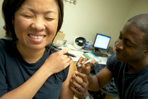 A woman winces while receiving a flu shot in the arm.