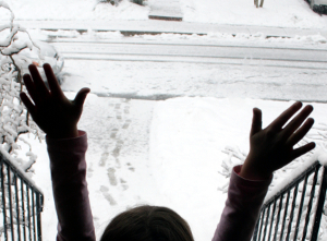 Young child in snowy landscape, hands held to the sky.