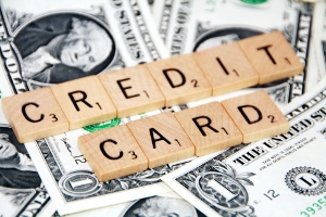 Credit cards spelled out by Scrabble pieces, atop fanned out dollar bills.